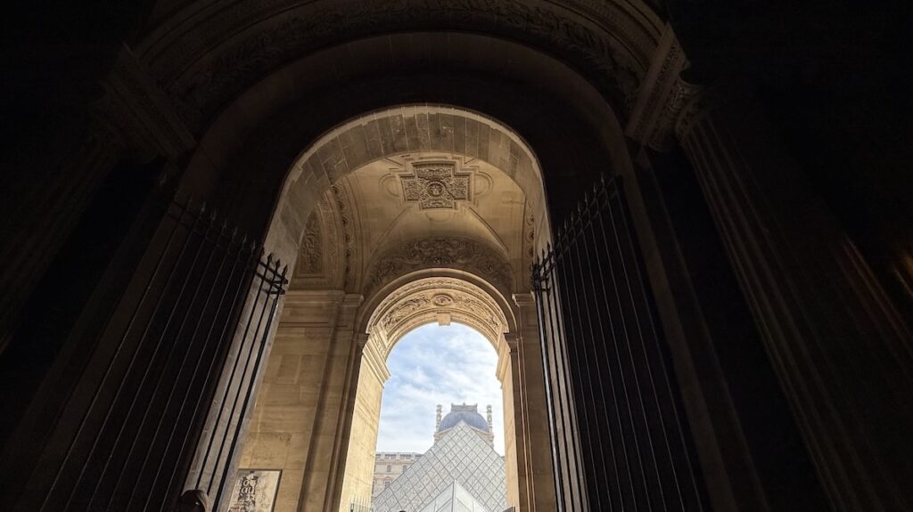 Pitch-dark arcade, glass pyramid ahead, Louvre building